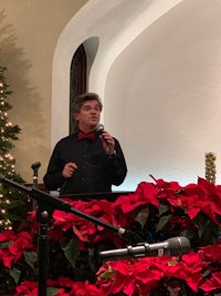 a man speaking into a microphone in front of poinsettias