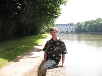 a man leaning against a wall next to a body of water