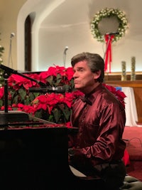 a man playing a piano in front of a christmas tree